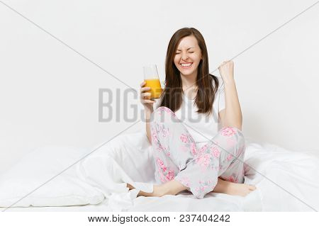 Young Brunette Woman Sits On Bed With White Sheet, Pillow, Wrapping In Blanket Isolated On White Bac