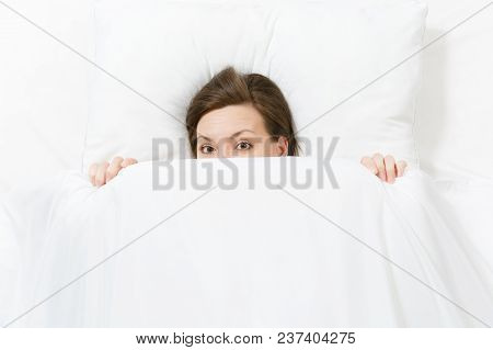 Top View Of Head Of Happy Brunette Young Woman Lying In Bed With White Sheet, Pillow, Blanket, Peek