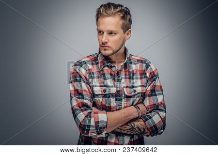 Studio Portrait Of Blond Male With Crossed Tattooed Arms, Dressed In A Plaid Shirt Isolated On Grey 
