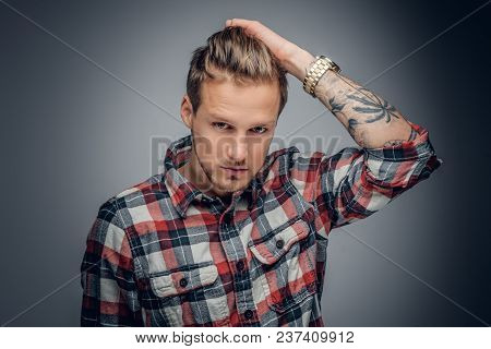 Portrait Of A Blond Male With Tattooed Arm On His Head Dressed In A Plaid Shirt Isolated On Grey Vig