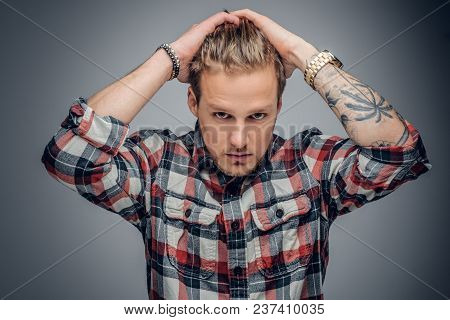 Portrait Of A Blond Male With Tattooed Arms On His Head Dressed In A Plaid Shirt Isolated On Grey Vi