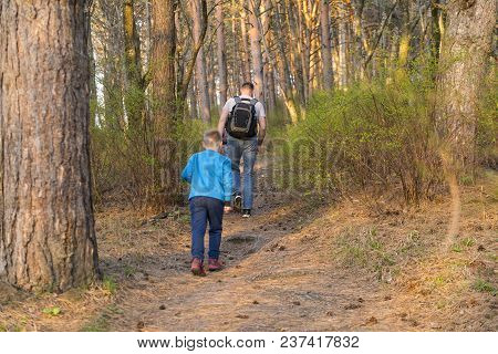 Father And Son Are Walking Together, People Are Walking Along A Path In The Forest Among Bushes And 