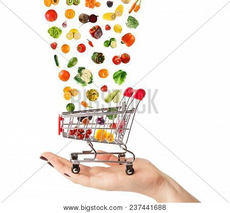 Female Hand Holding Grocery Cart With Vegetables And Fruits Falling In It Isolated On White. Healthy