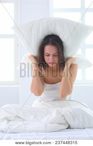 Young caucasian woman covering her head and ears with pillows