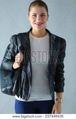 portrait of beautiful young brunette woman in stylish black jacket on gray.