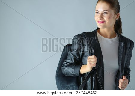 portrait of beautiful young brunette woman in stylish black jacket on gray.