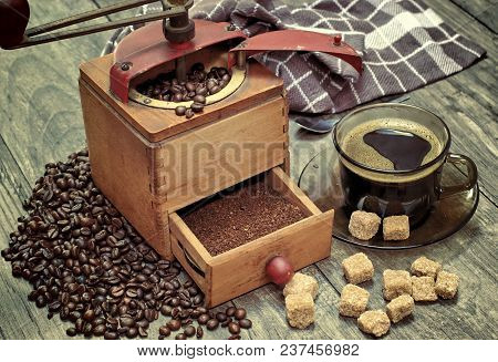 Old Coffee Grinder With A Cup Of Coffee, Coffee Beans On A Wooden Background.