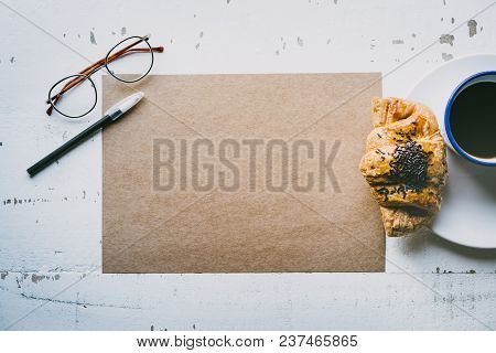 Mockup Blank Craft Sheet Of Blank Craft Paper, Pen, Eye Glasses And Morning Coffee Cup With Croissan