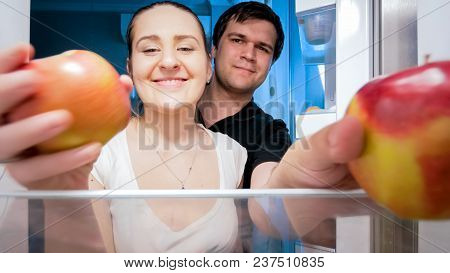 Portrait Of Smiling Couple Taking Apples From Refrigerator At Night