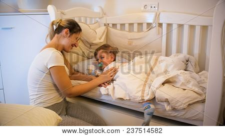 Mother Caressing Her Crying Toddler Son Lying In Bed At Night