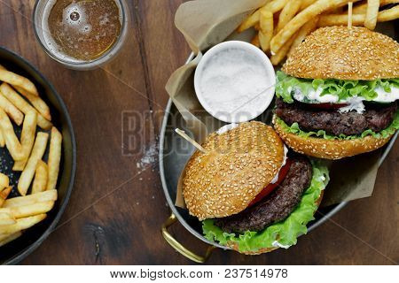 Top View Burgers, French Fries, Sauce Served In Frying Pans On Wooden Table With Beer, Top View