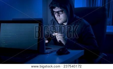 Male Hacker Holding Credit Card And Typing Fraud Program Code On Laptop