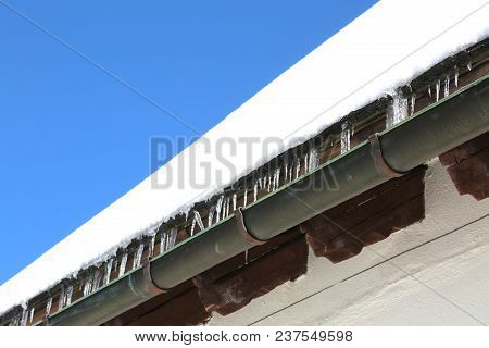 Gutter With Icicles Of Ice On The Roof After Copious Winter Snowfall