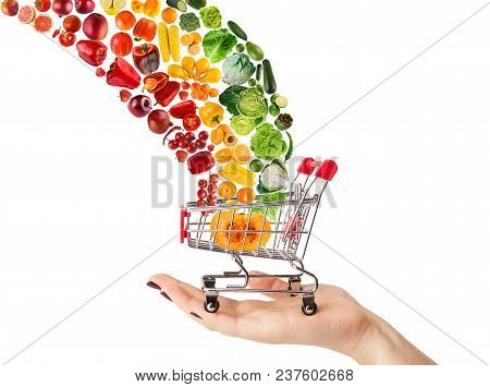 Female Hand Holding Grocery Cart With Vegetables And Fruits Falling In It Isolated On White. Healthy