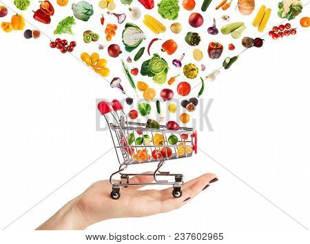 Female Hand Holding Grocery Cart With Vegetables And Fruits Falling In It Isolated On White. Healthy
