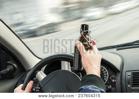 Opened Bottle Of Beer And Hands On The Steering Wheel Of A Car