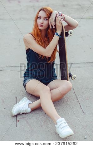 Redhead Slim Girl In Jeans Shorts And Black T Shirt Posing With Skateboard In Urban Sciene.
