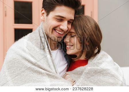 Portrait of beautiful couple in love smiling and hugging together outside cafe wrapping in one blanket