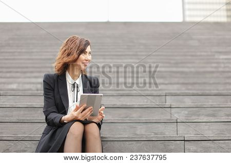 Young Businesswoman Sitting On Stairs With Tablet. Concept Of Working In Open Ait And Modern Technol