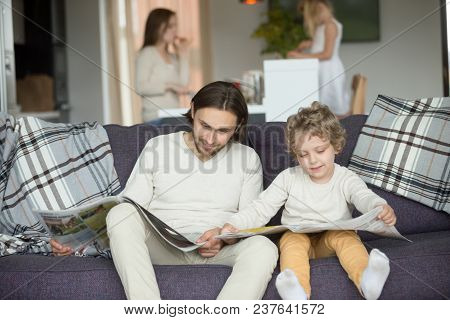Little Son Pretending Reading Newspaper Sitting On Couch With Father, Cute Funny Kid Imitating Dad T