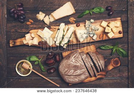 Cheese Platter With Different Cheeses, Grapes, Nuts, Honey, Bread And Dates On Rustic Wooden Backgro