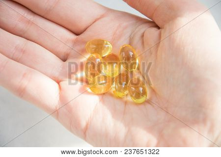 Hand With Capsules Of Yellow Fish Oil Vitamins On White Background.