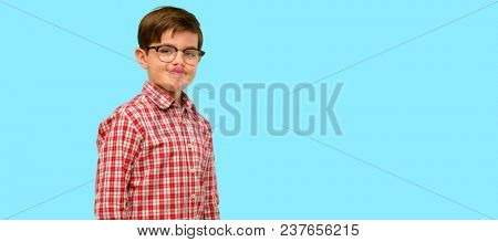 Handsome toddler child with green eyes sticking out tongue at camera at sign of disobedience, protest and disrespect over blue background