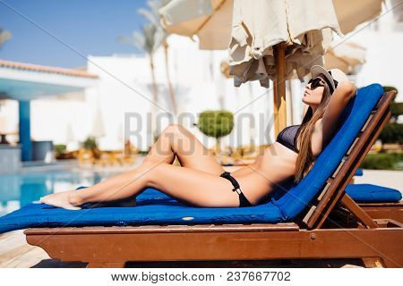 Happy Young Woman Relaxing On Sun Bed By The Pool