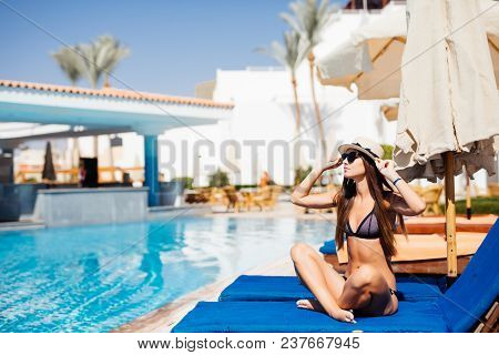 Happy Young Woman Relaxing On Sun Bed By The Pool