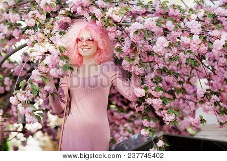 Beautiful Young Woman With Curly Pink Hair And Sunglasses Near The Blossoming Spring Tree