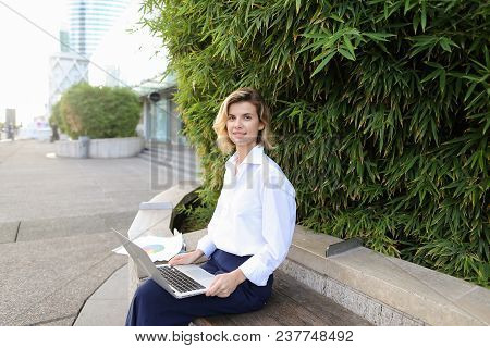Caucasian Businesswoman Working With Laptop And Papers In Open Air Near Green Plant. Concept Of Busi