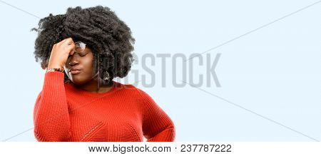 Beautiful african woman with sleepy expression, being overworked and tired, rubbes nose because of weariness, blue background