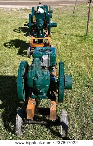 Two Old Similar Restored Gas Engines With Heavy Fly Wheels Mounted On Portable Carts Used To Power M