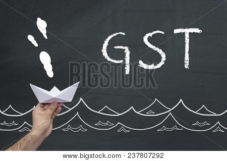 Gst Concept. Male Hand Holding Paper Boat On Blackboard With Inscription Gst.