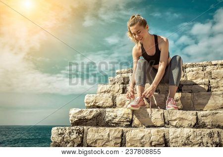 Women runner bootlace on her boot after running in sunny day under sunlight from blue sky near the sea.