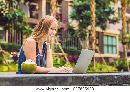 Young Female Freelancer Sitting Near The Pool With Her Laptop In The Hotel Browsing In Her Smartphon