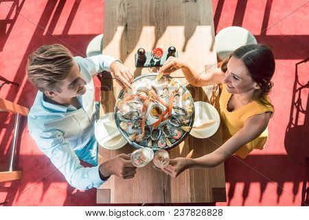 High-angle view of a happy young couple toasting with champagne during romantic dinner with fresh seafood at a trendy restaurant