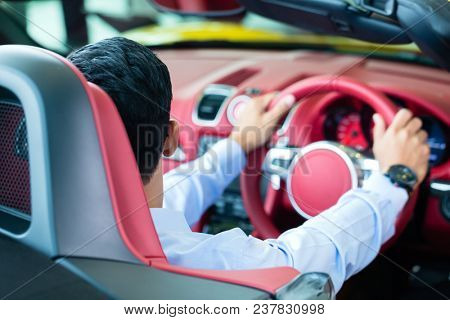 Asian man testing new sports car at car dealership