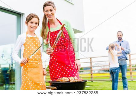 Mother and Son barbecue meat spits and sausages at family garden BBQ 
