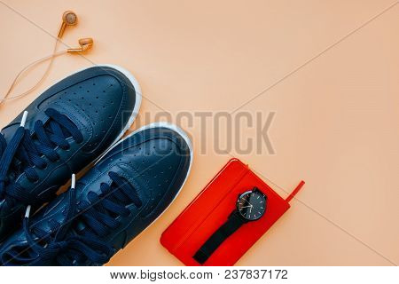 Flatlay Of Casual Style Dark Blue Leather Sneakers With Rose Gold Earphones, Red Notebook, Black Dia