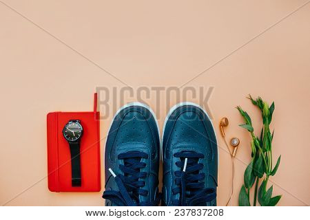Flatlay Of Casual Style Dark Blue Leather Sneakers With Rose Gold Earphones, Red Notebook, Black Dia