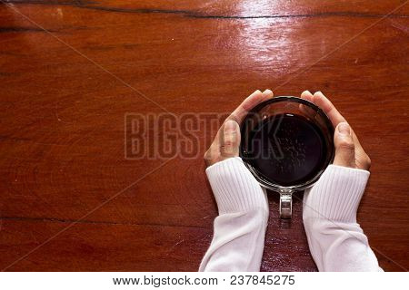 A Woman Holding A Cup Of Coffee On A Wooden Background.