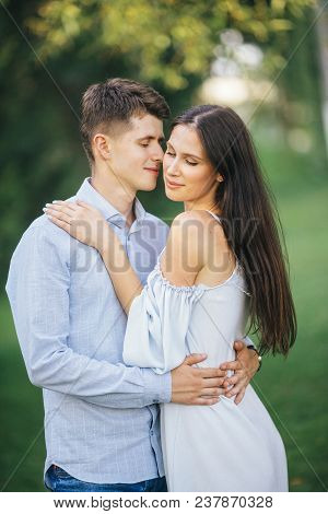 Happy Loving Couple Stay And Hugging At Park Background Lake. Young Cople That Is About To Kiss. Sum