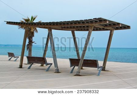 Wooden Shade Structure With Seats, Blue Mediterranean Sea On An Overcast Day And Horizon In Molinar,