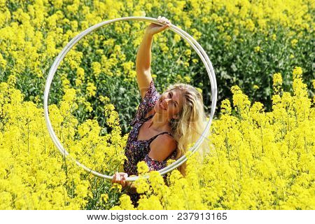 Blonde Peasant Girl In Floral Print Dress With Hula-hoop On The Yellow Blossoming Rapeseed Field