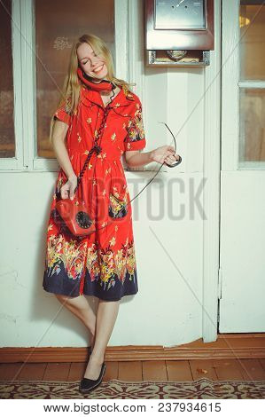 Beautiful Blond Woman With An Old Wired Phone Dressed In A Red Dress, Standing In An Old House, Vint