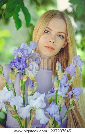 Attractive Young Girl With Blonde Dren Hair And Natural Make-up Smelling Blue Purple Iris Flowers On