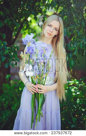 Attractive Young Girl With Blonde Dren Hair And Natural Make-up Smelling Blue Purple Iris Flowers On
