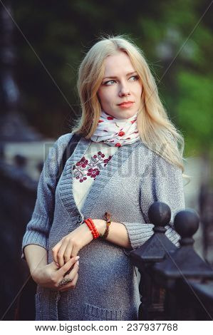 Beautiful Blond Woman Standing In The City At Night Dressed In A White Dress And A Sweater On Her Ne