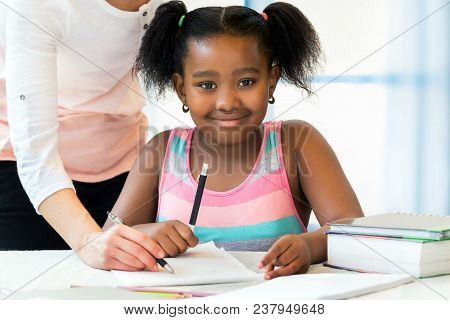 Close Up Portrait Of Cute Little African Student Doing Homework With Caucasian Teacher. Pony Tailed 